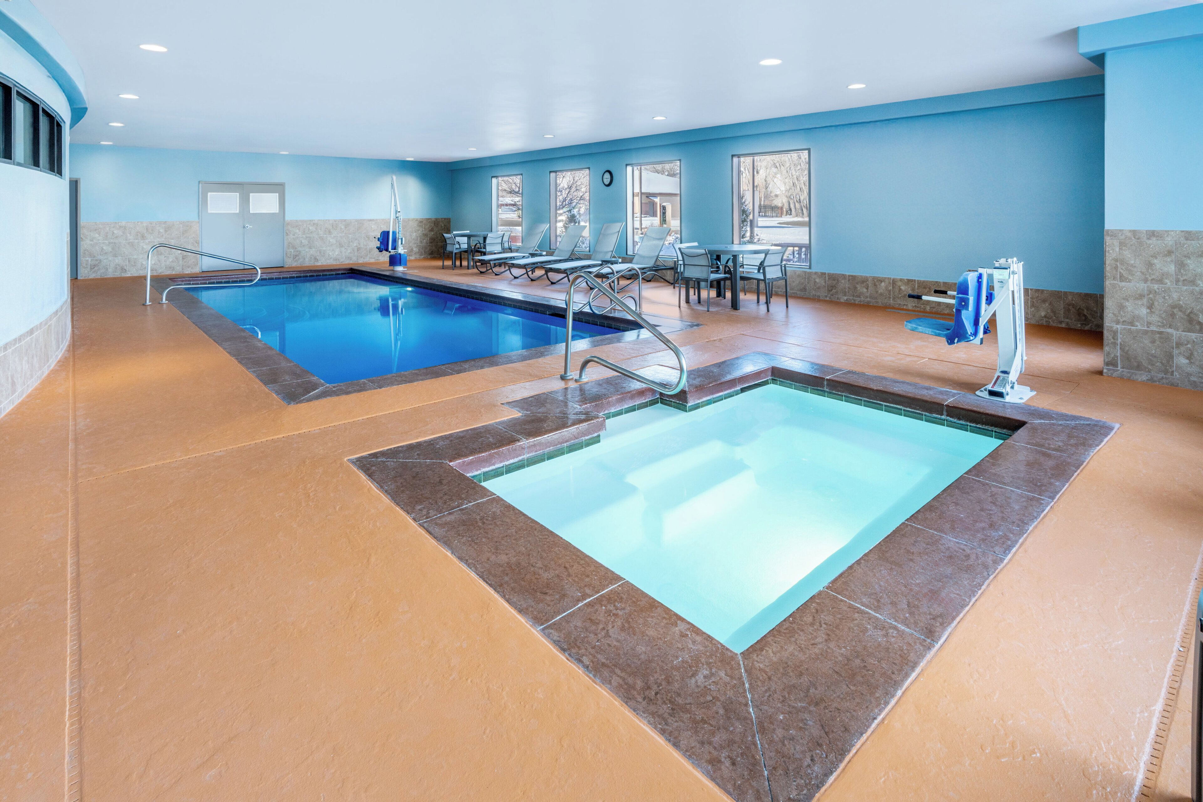 Un área de piscina con dos piscinas, sillas de descanso y una mesa.