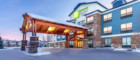 Edificio de Holiday Inn Express & Suites con entrada cubierta y pilares de piedra.