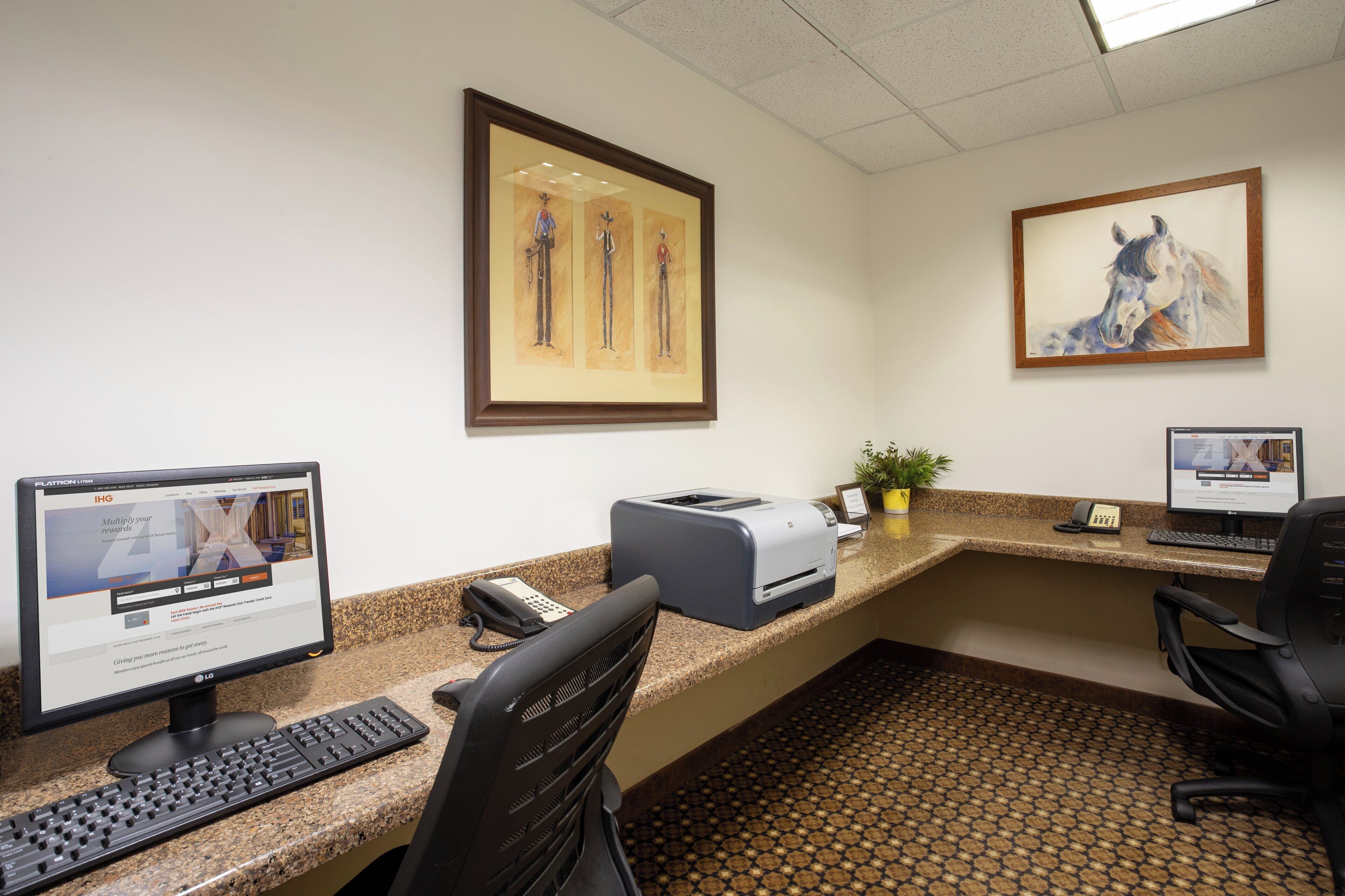 A hotel reception desk with computers, a printer, and framed artwork on the wall.