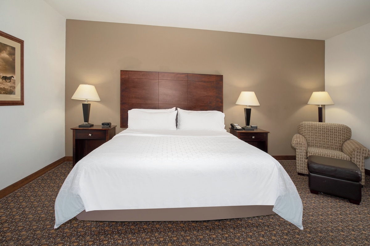 A hotel room with a large bed, two bedside tables with lamps, a chair, and a carpeted floor.