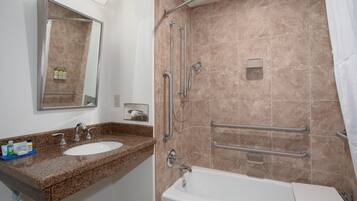 Un baño con lavamanos, espejo, ducha y barras de apoyo.