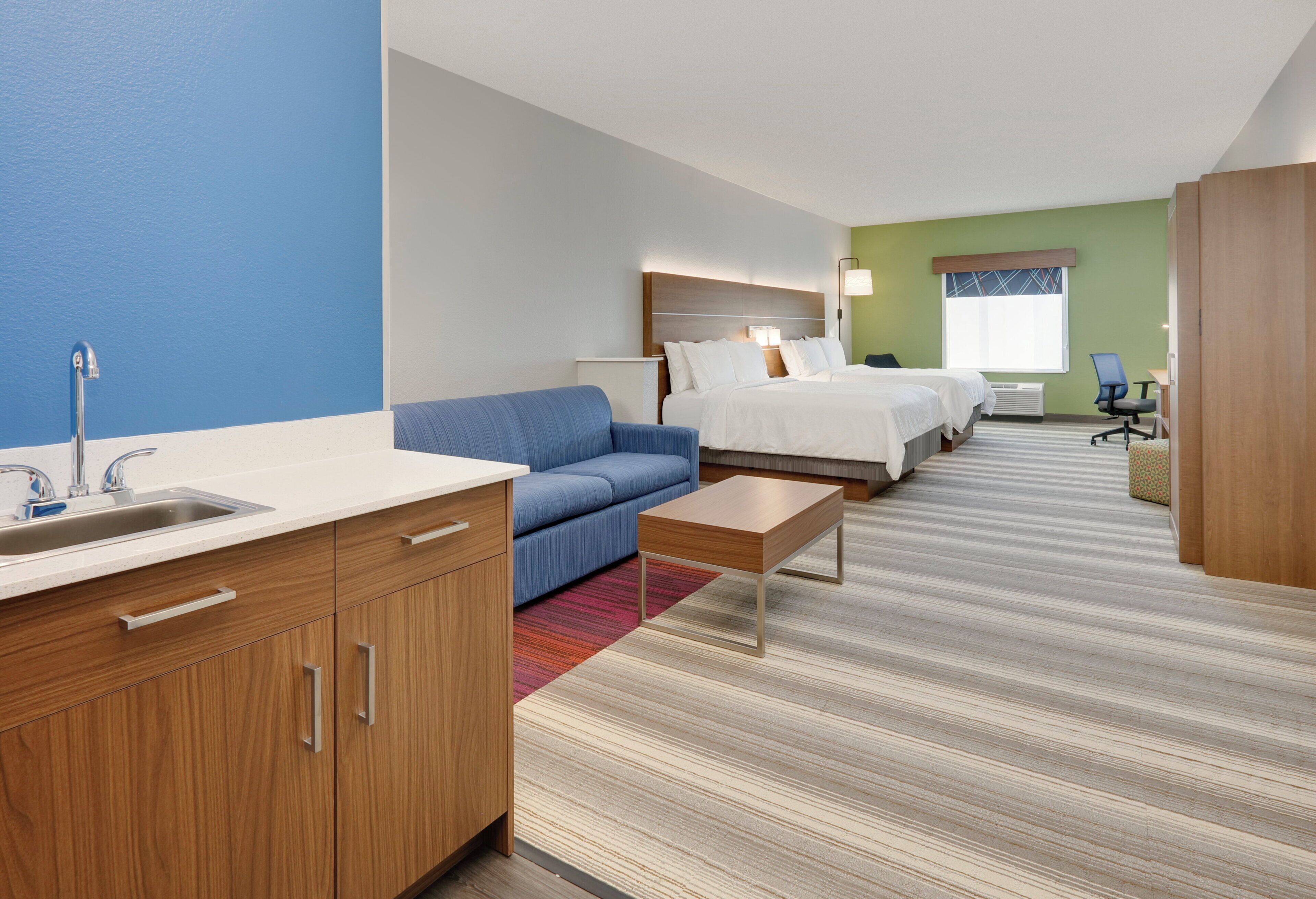 A hotel room with a kitchenette, a sofa, a bed, a desk, and a window.