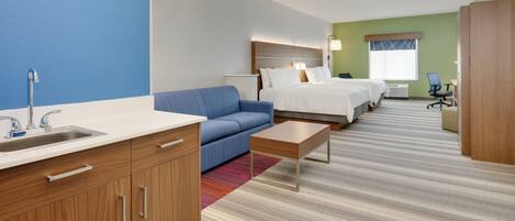 A hotel room with a kitchenette, a sofa, a bed, a desk, and a window.