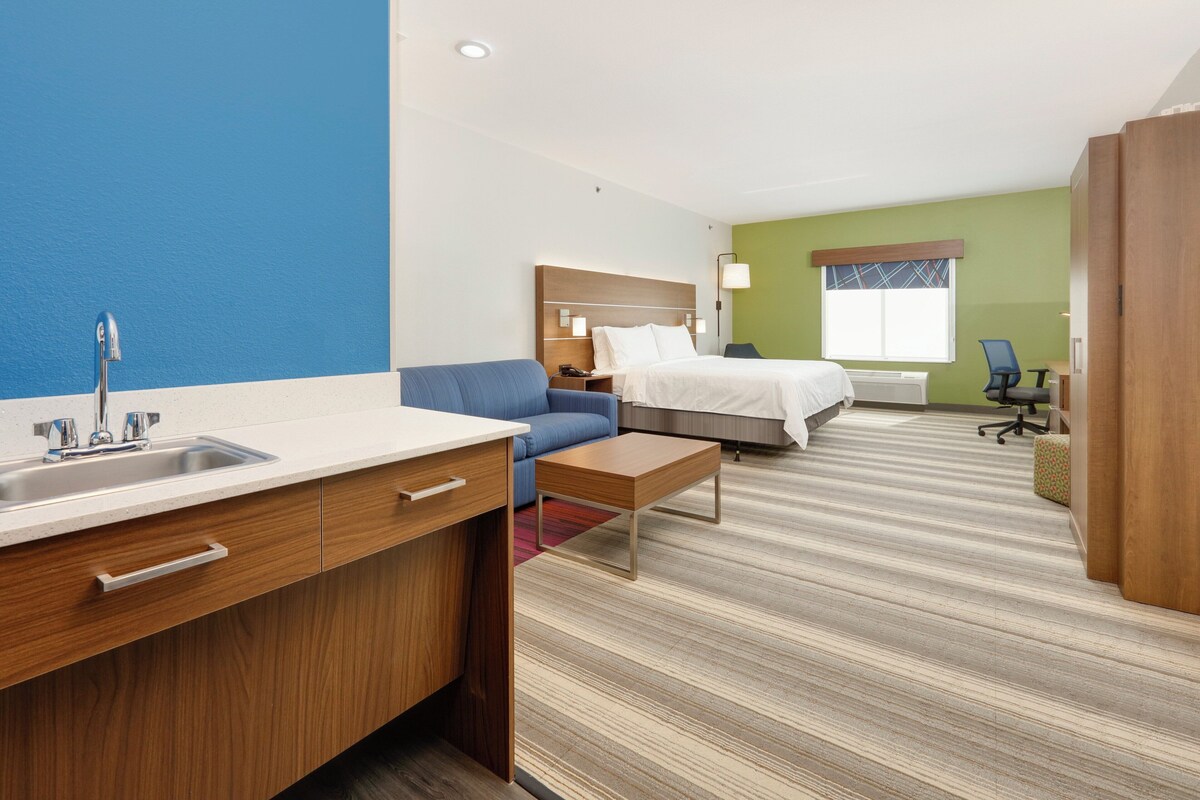 A hotel room with a kitchenette, a bed, a desk, and a chair.
