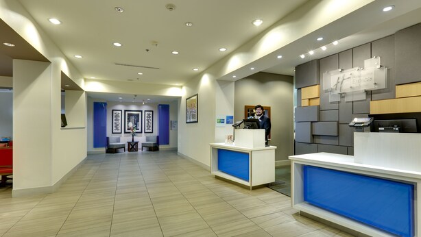 A modern reception area with a receptionist desk, a blue accent wall, and a reception desk with a digital screen. - Holiday Inn Express & Suites Denton North by IHG (Denton)