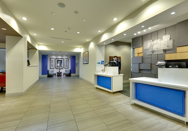 A modern reception area with a receptionist desk, a blue accent wall, and a reception desk with a digital screen. - Holiday Inn Express & Suites Denton North by IHG (Denton)