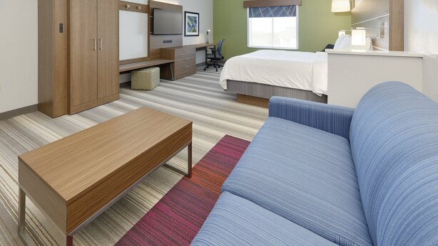 A hotel room with a bed, a sofa, a desk with a chair, a wardrobe, and a television. - Holiday Inn Express & Suites Denton North by IHG (Denton)
