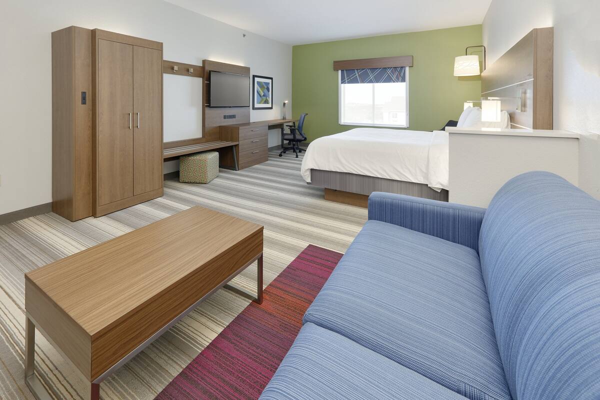 A hotel room with a bed, a sofa, a desk with a chair, a wardrobe, and a television.