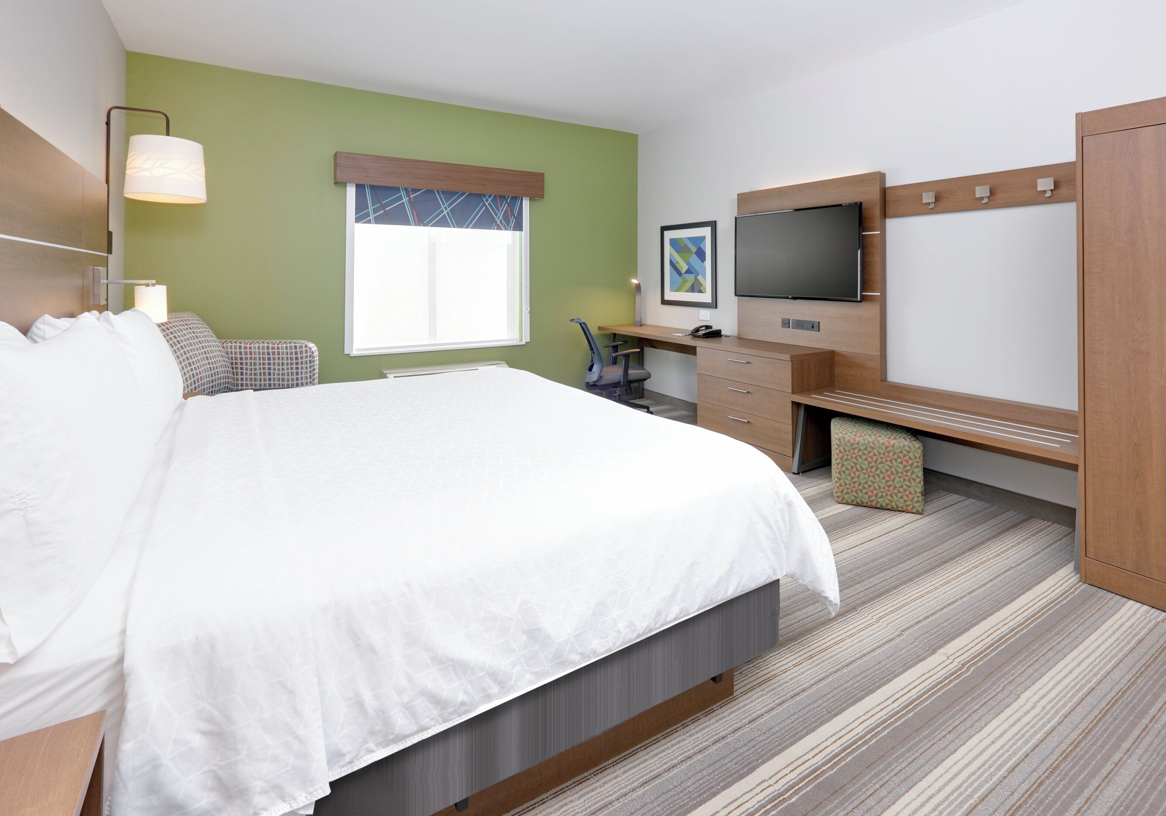 A hotel room with a bed, desk, chair, television, and a window.
