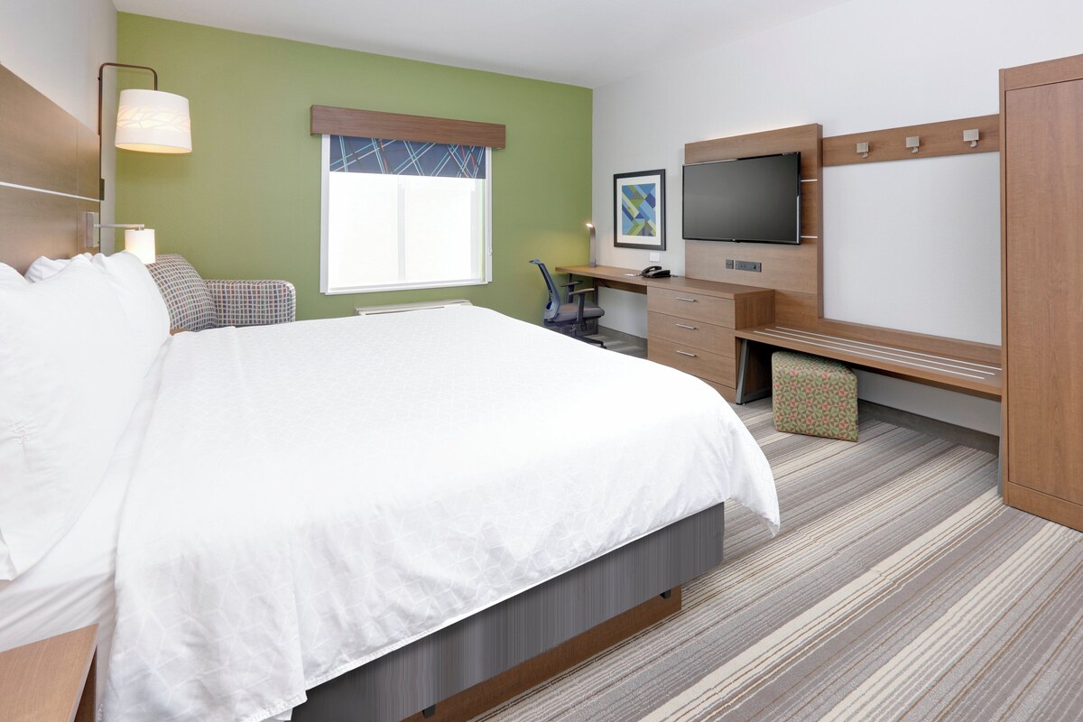 A hotel room with a bed, desk, chair, television, and a window.