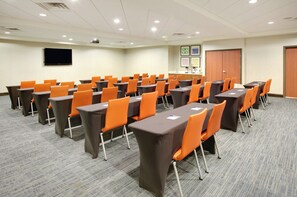 A conference room with rows of tables and chairs, a projector screen, and a door with a cabinet. - Holiday Inn Express & Suites Denton North by IHG (Denton)