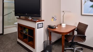 Habitación de hotel con televisión, escritorio con silla, un bote de basura y una lámpara fijada a la pared.
