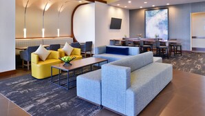 A modern hotel lobby with a seating area, a dining table, and a large screen. - Hyatt Place Garden City (Garden City)
