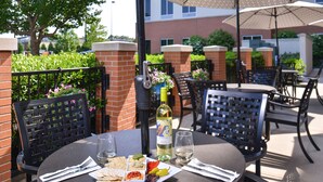 An outdoor dining area with tables and chairs, a bottle of wine, and a plate of food. - Hyatt Place Garden City (Garden City)
