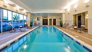 An indoor swimming pool with clear blue water, lounge chairs, and a view of the parking lot through large windows. - Hyatt Place Garden City (Garden City)