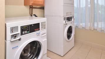 A laundry room with a front-loading washer and dryer, wooden cabinets, and a window with curtains.