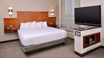 A hotel room with a large bed, two bedside tables, a flat-screen TV, and a minibar.