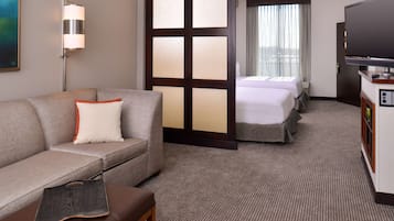 A hotel room with a sofa, a desk, a TV, and two beds.
