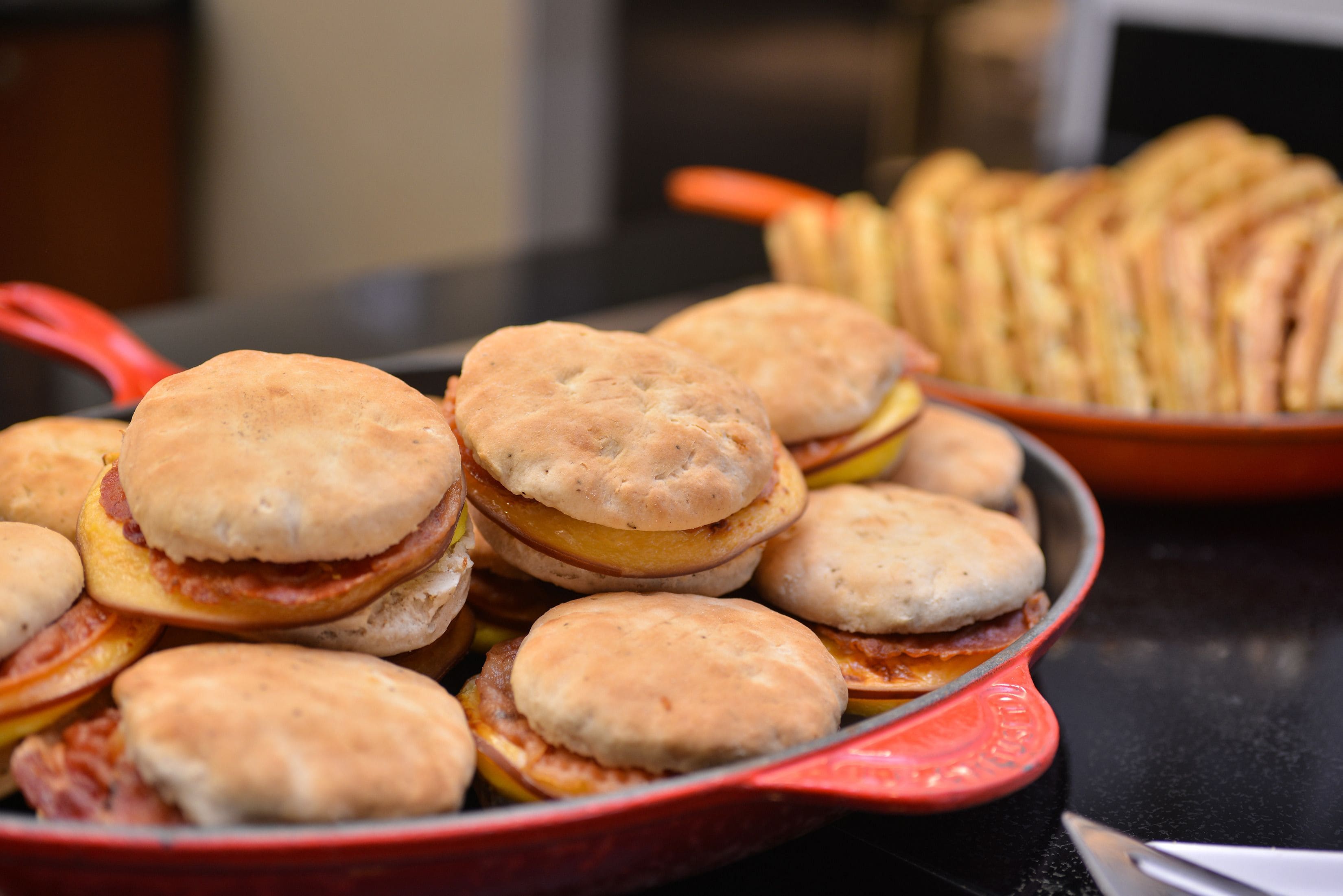 A red skillet filled with breakfast sandwiches and a plate of biscuits.