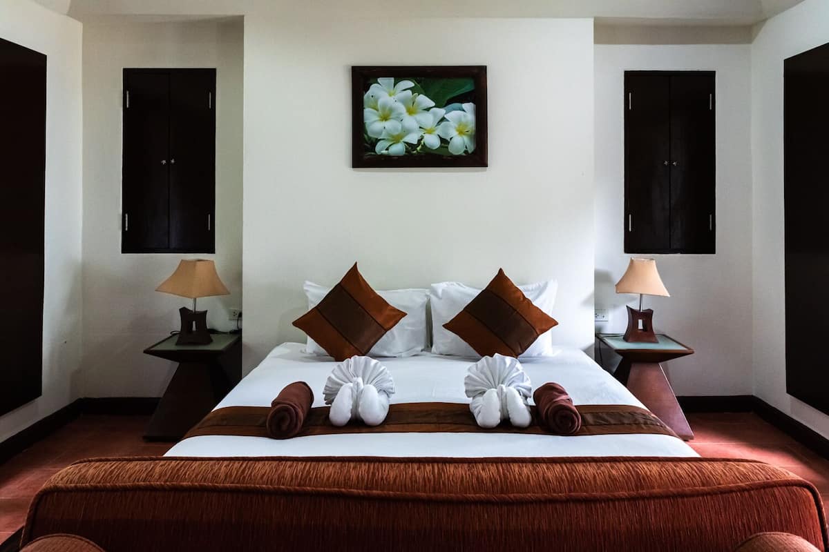 A hotel room with a large bed, two nightstands, a wall-mounted TV, and a framed floral artwork above the bed.