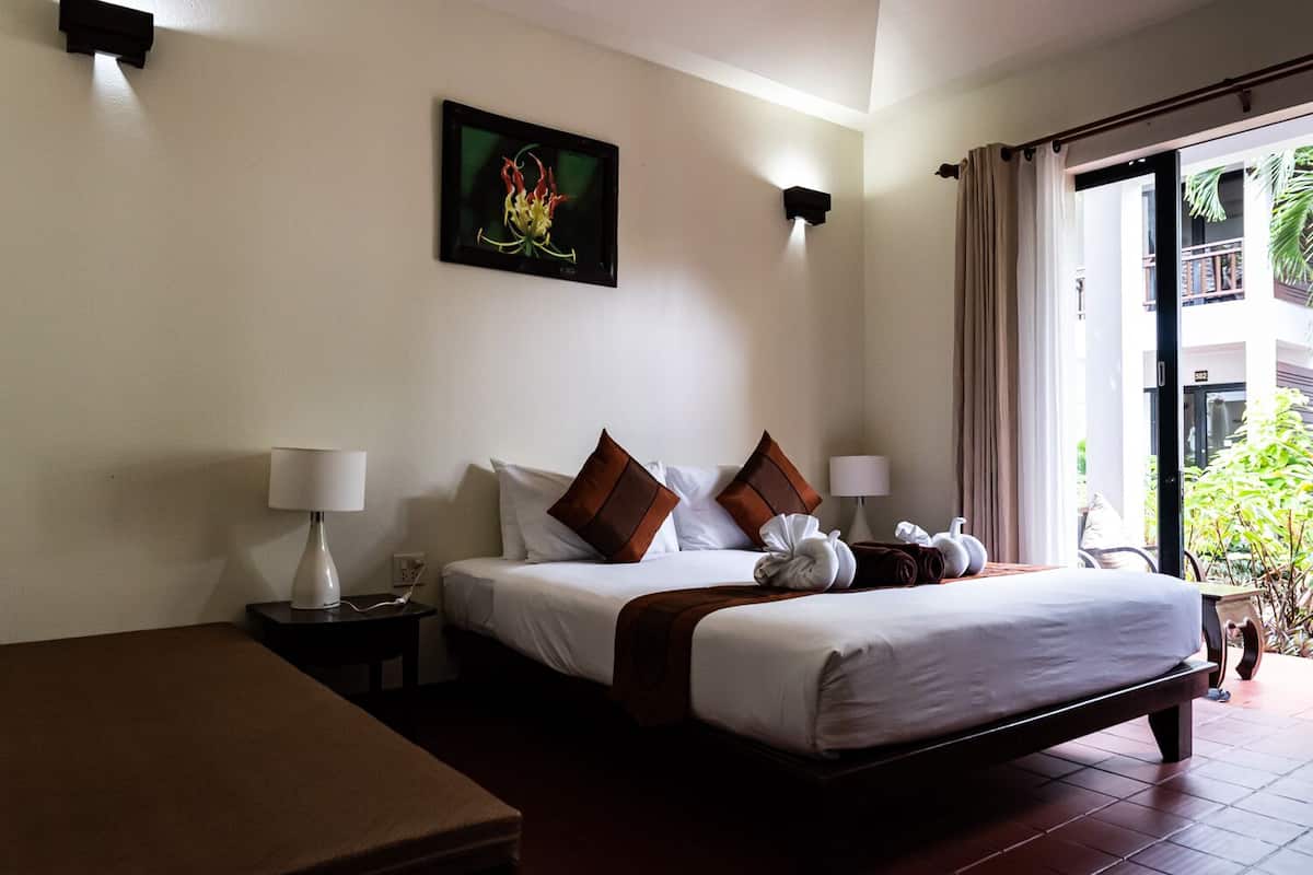 A hotel room with a bed, two bedside tables, a nightstand, a window with curtains, and a wall-mounted picture.