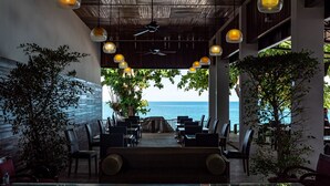 An outdoor dining area with tables and chairs, a ceiling fan, and hanging pendant lights. - The Hive Hotel Samui (Koh Samui)