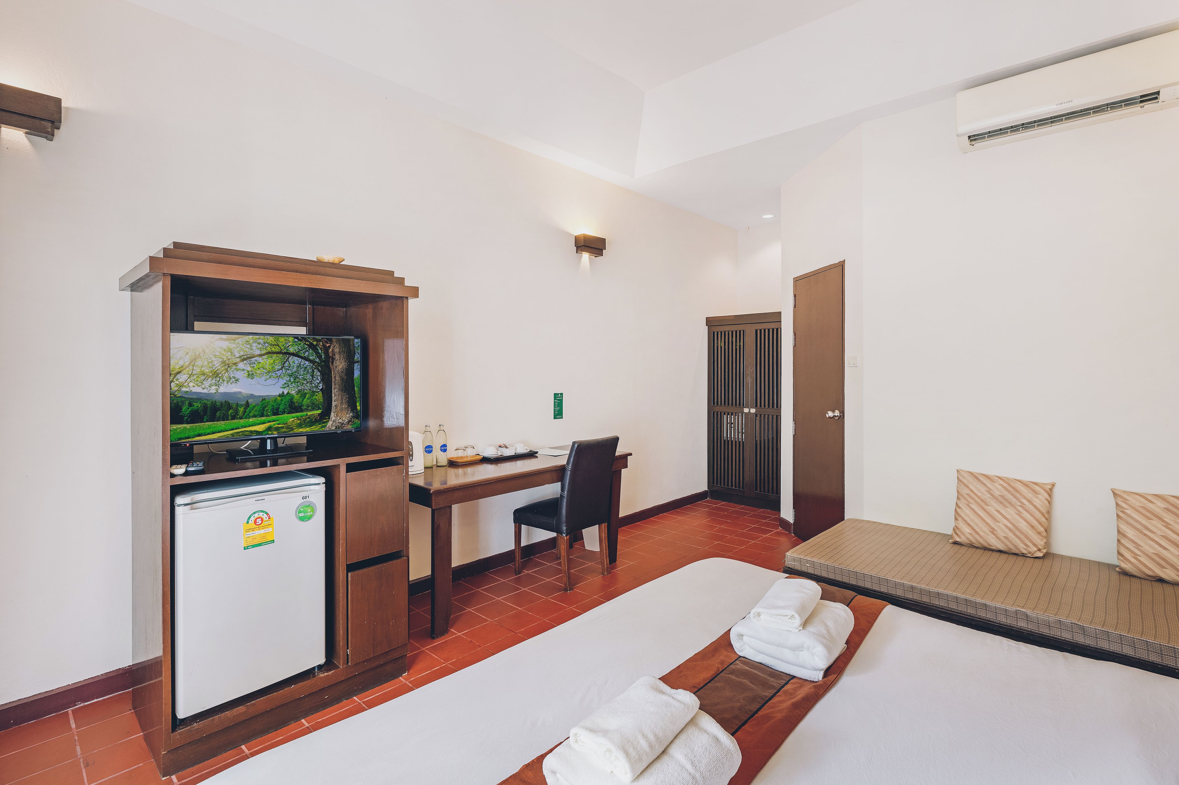 A hotel room with a bed, a desk with a computer, a television, and a minibar.
