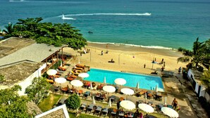 A pool area with lounge chairs and umbrellas, a beach with people, and a view of the ocean. - The Hive Hotel Samui (Koh Samui)