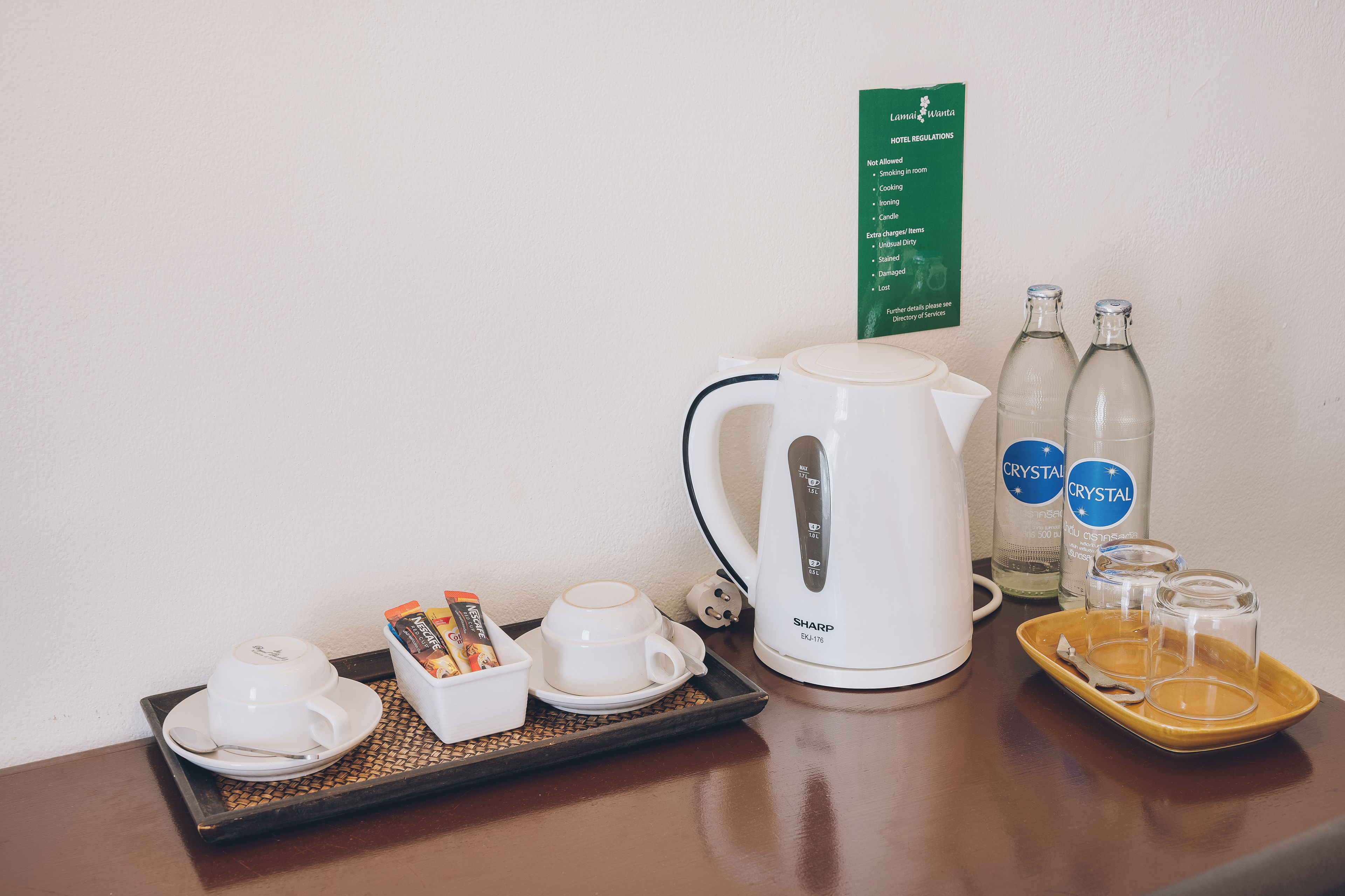 Habitación de hotel con cafetera, dos tazas, una bandeja con cápsulas de café, dos botellas de agua y un cartel con las normas del hotel.