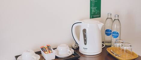 Habitación de hotel con cafetera, dos tazas, una bandeja con cápsulas de café, dos botellas de agua y un cartel con las normas del hotel.