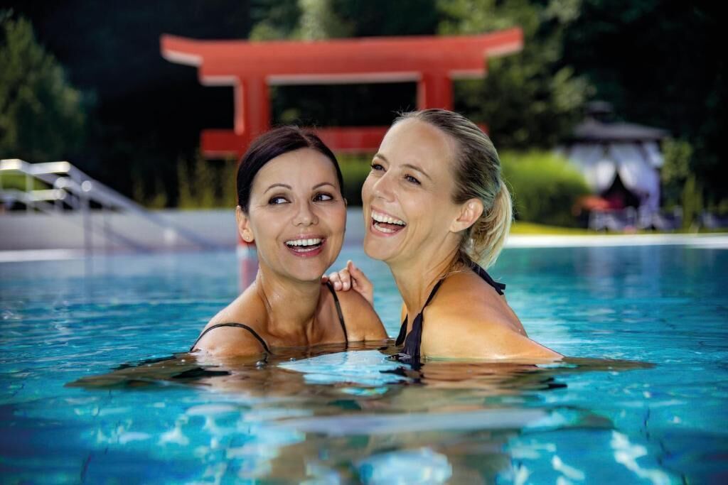 Two people in a swimming pool with a red structure in the background.