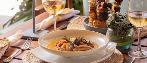 A dining table with a plate of seafood, two glasses of white wine, and a bowl of soup.
