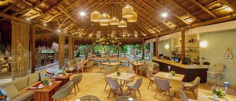 A spacious indoor area with wooden furniture, a thatched roof ceiling, and a bar area.