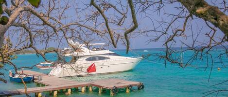 A yacht docked at a pier with clear turquoise water and a view of the sea.