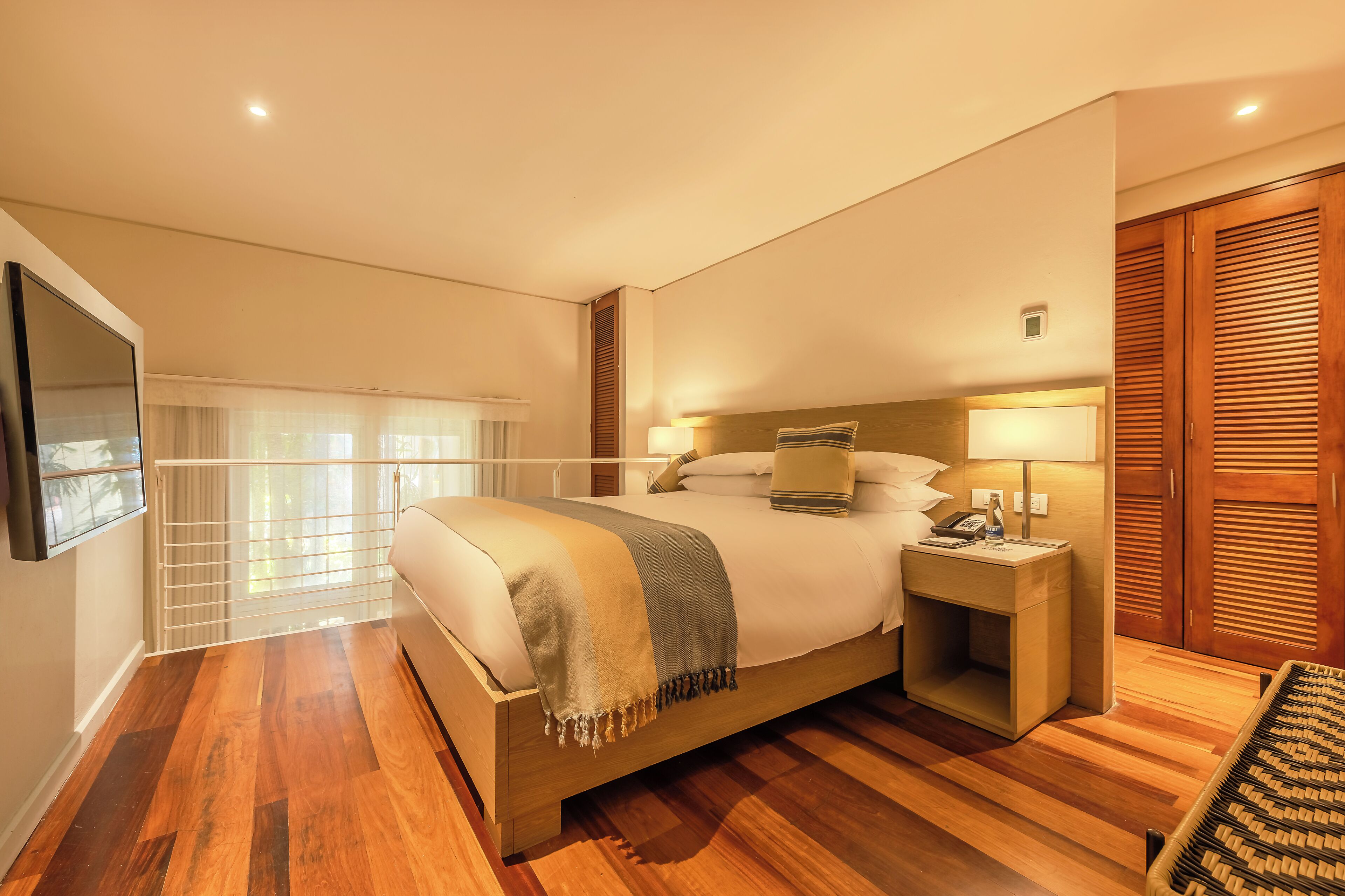 A spacious bedroom with a large bed, bedside lamps, a wooden headboard, and a wooden floor.