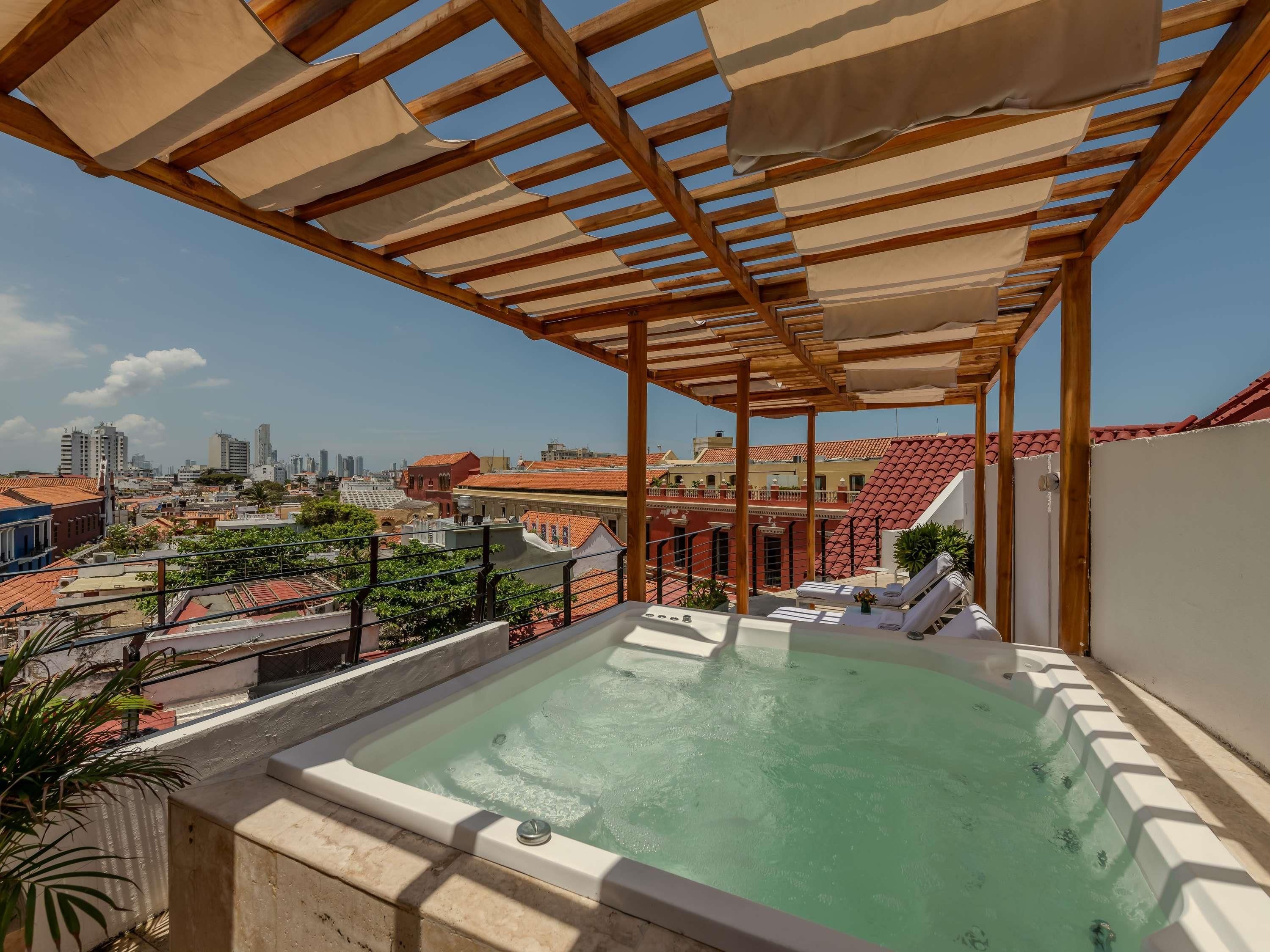 Una piscina en la azotea con una pérgola, sillones de descanso y vistas a la ciudad.