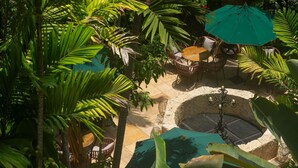 An outdoor seating area with tables and chairs, surrounded by lush greenery and a central decorative feature.