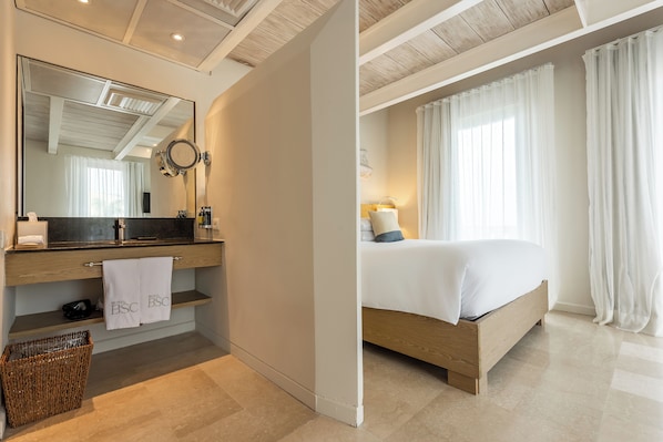 A hotel room with a wooden bed, a large mirror, a wooden vanity, a towel rack, and a wicker basket.