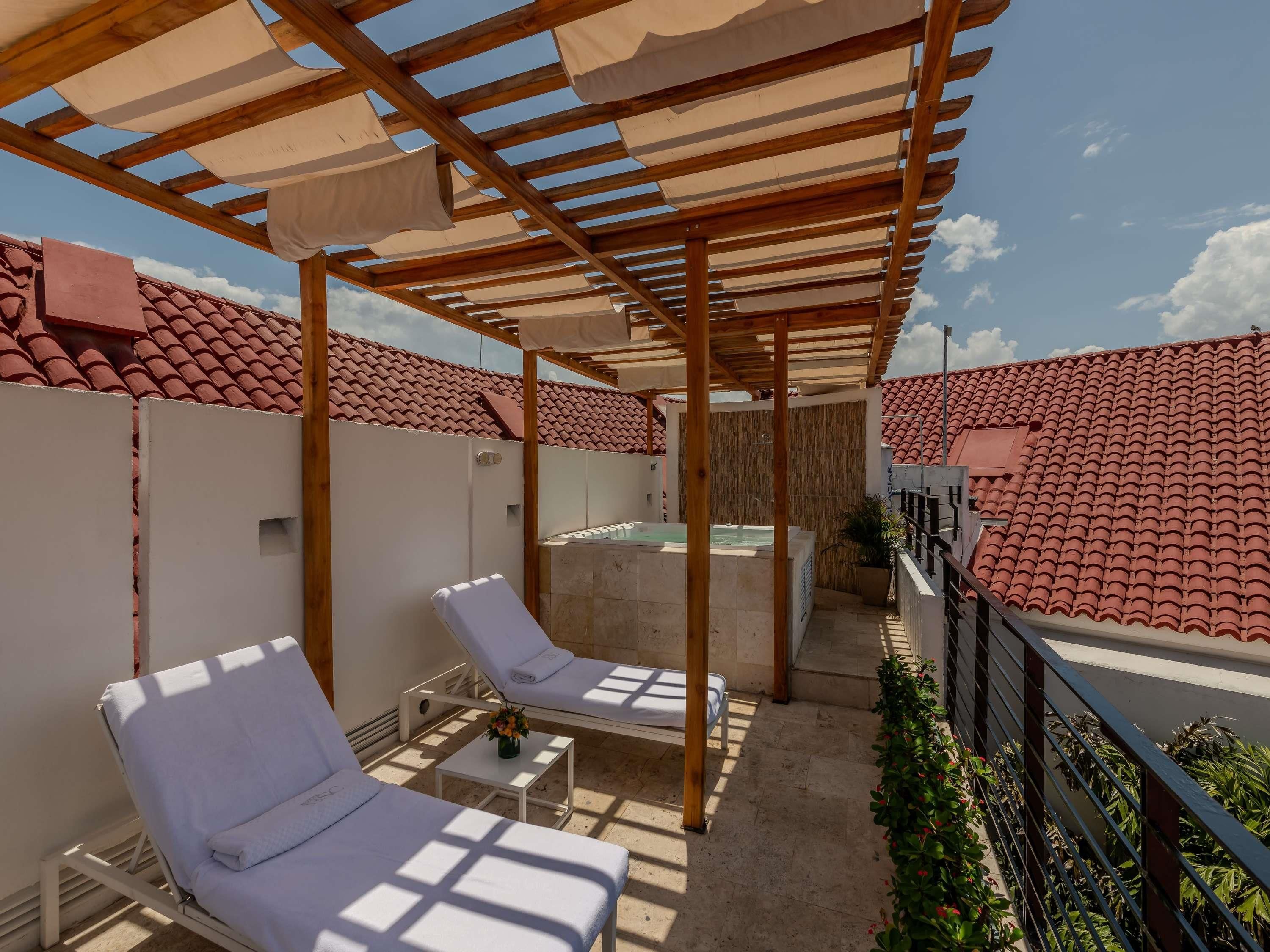 A rooftop terrace with two sun loungers, a small table with a vase, and a hot tub.