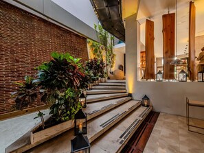 A staircase with wooden steps, surrounded by plants and lanterns, leading to a room with a brick wall and wooden beams.