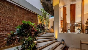 A staircase with wooden steps, surrounded by plants and lanterns, leading to a room with a brick wall and wooden beams.