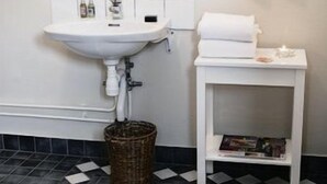 A bathroom with a white sink, tiled floor, and a small white table with towels. - Hotel Bakfickan (Stockholm)