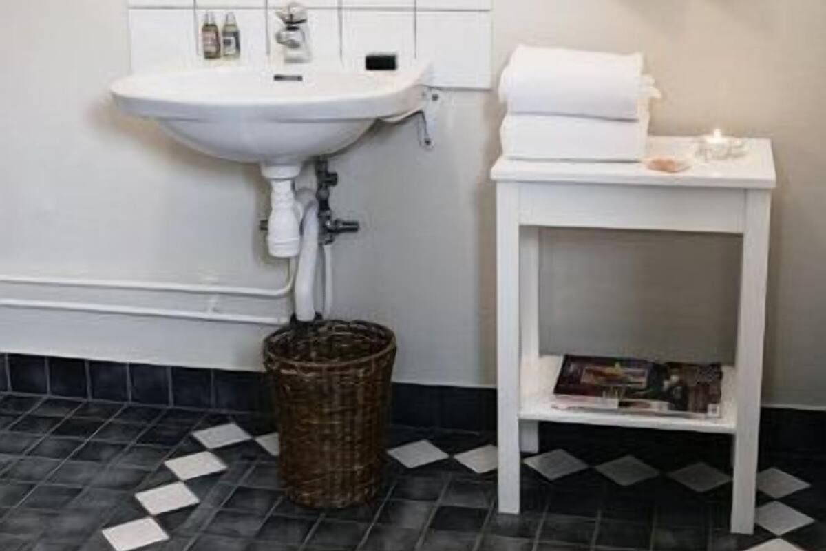 A bathroom with a white sink, tiled floor, and a small white table with towels.