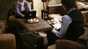 A room with a wicker sofa, a small table with a laptop and a book, and a suitcase on the floor. - Hotel Bakfickan (Stockholm)