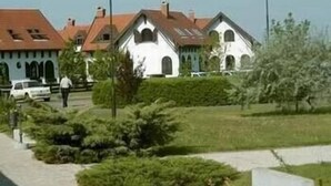 A row of white buildings with red roofs, likely residential or institutional, with a paved pathway and greenery in front.