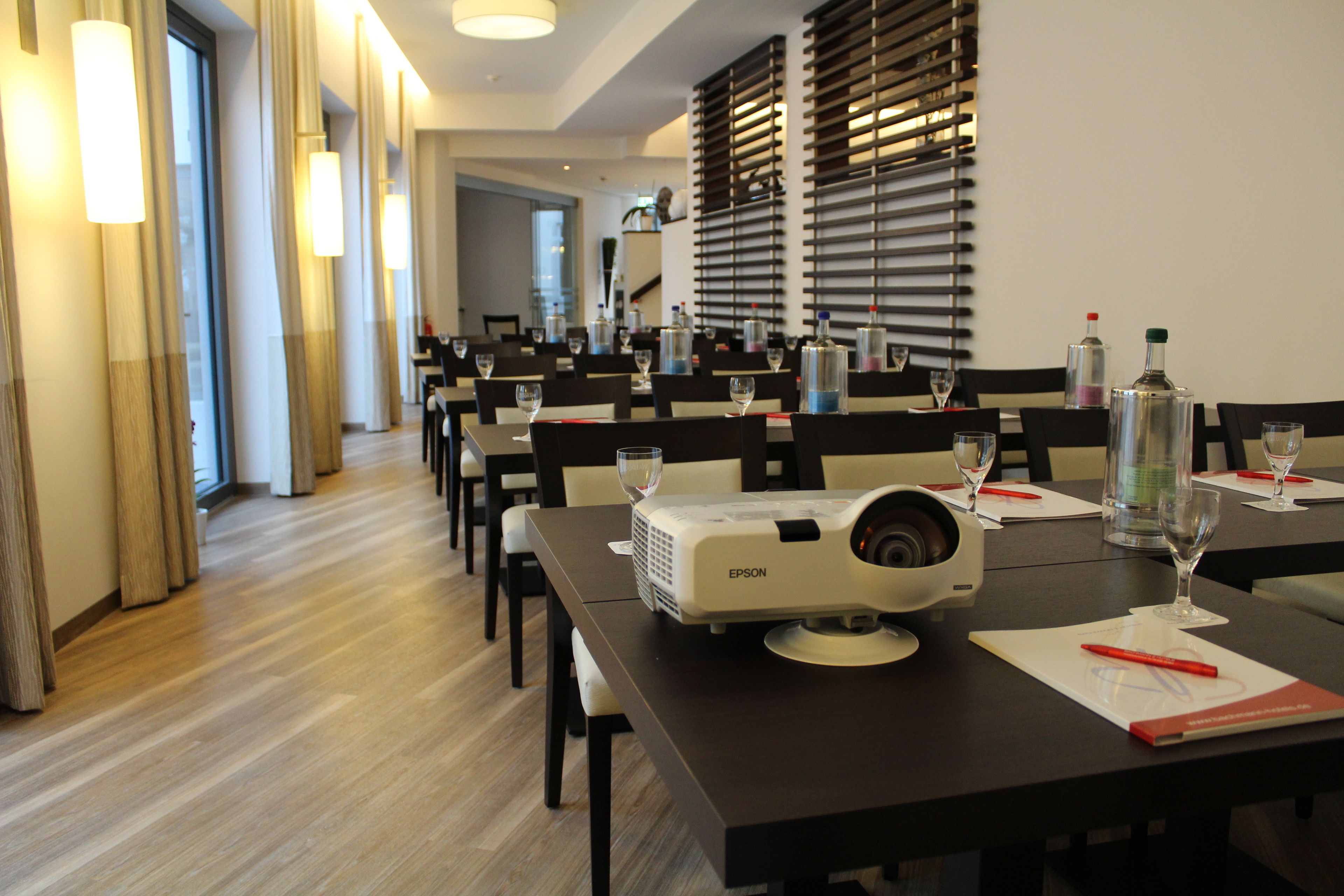 A conference room with a projector, tables, chairs, and a large window.