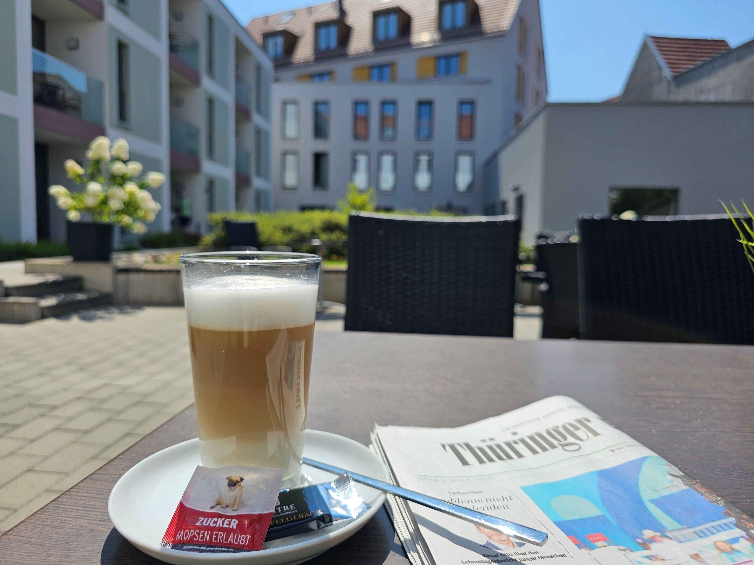 A glass of beer on a saucer with a newspaper and a packet of snacks on a table.
