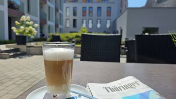 A glass of beer on a saucer with a newspaper and a packet of snacks on a table.