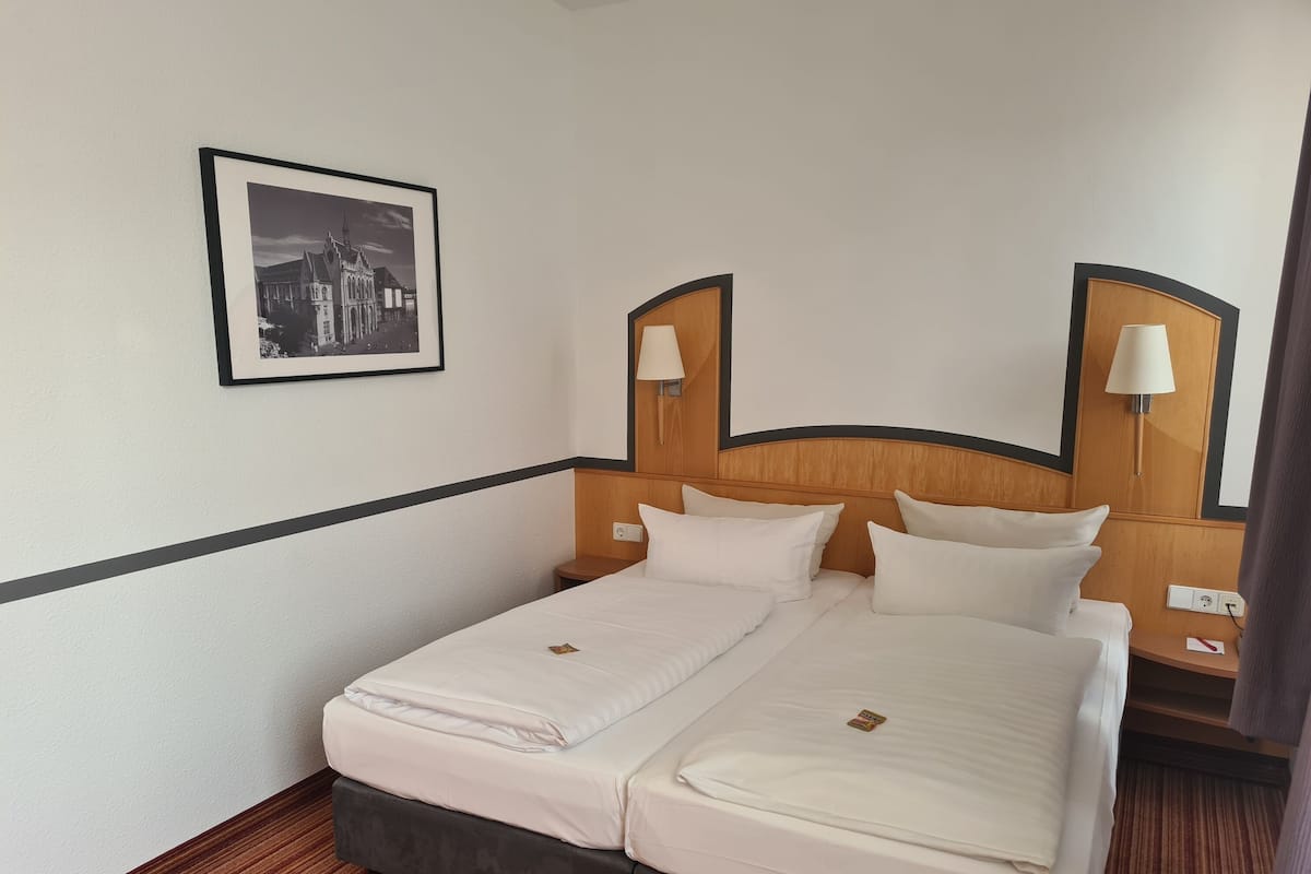 Ein Hotelzimmer mit Doppelbett, zwei Nachttischen, einer Lampe und einem gerahmten Bild an der Wand.