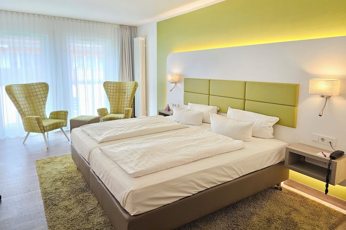 Ein Hotelzimmer mit einem großen Bett, zwei Sesseln, einem Nachttisch und einer Lampe.